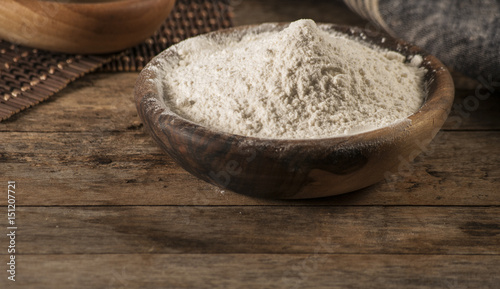 Flour in a wooden bowl, paper bag and spoon. Top view, space for text.