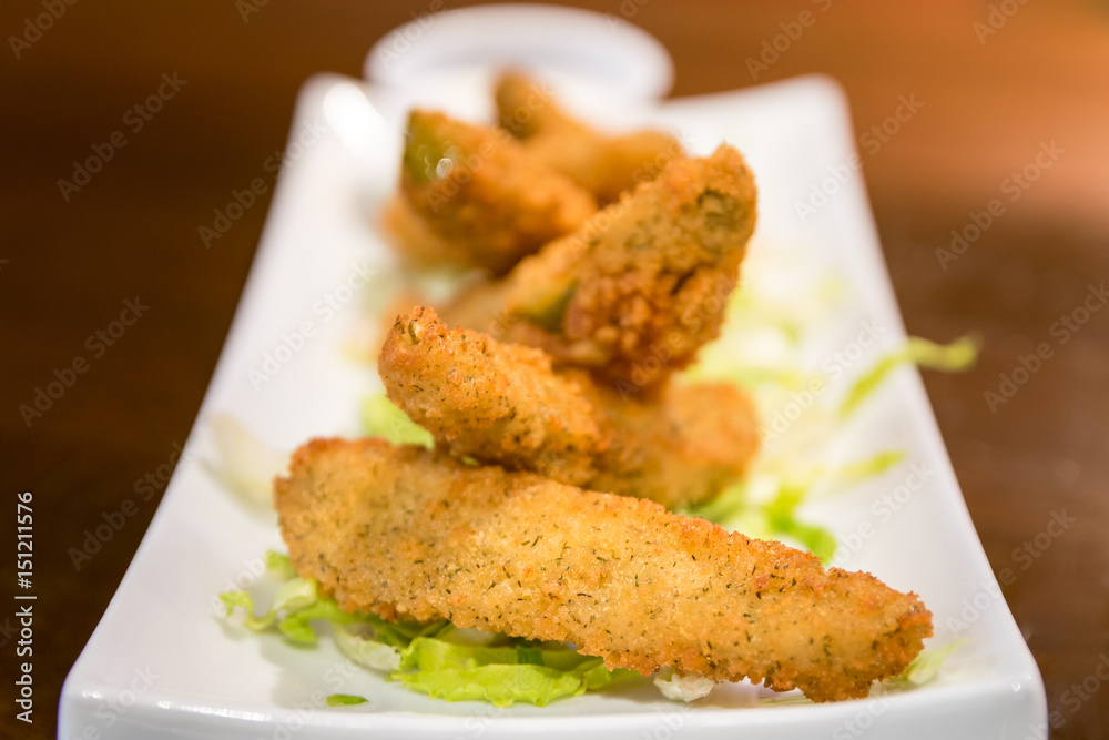 Delicious deep fried dill pickle spears, served with sour cream on a white plate.
