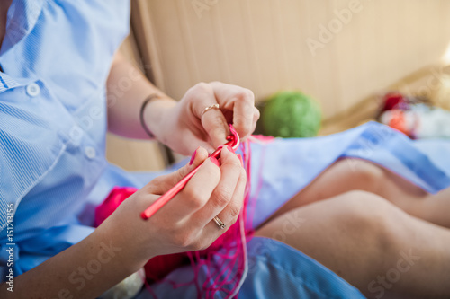 A girl in a blue dress crochets. Hands hold knitting
