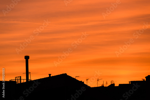 Red sky sunset with clouds, roofs, antennas and plane in back light photo