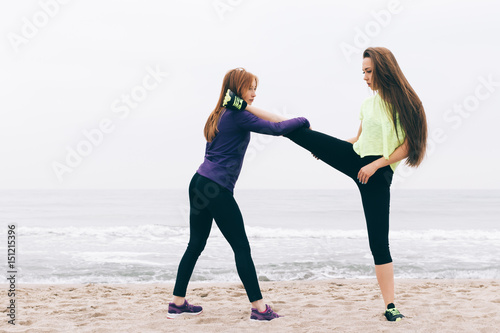 Girls in sportswear are stretched on the beach