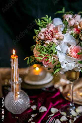 graceful table layout with a bouquet from roses and carnations, and the burning candle