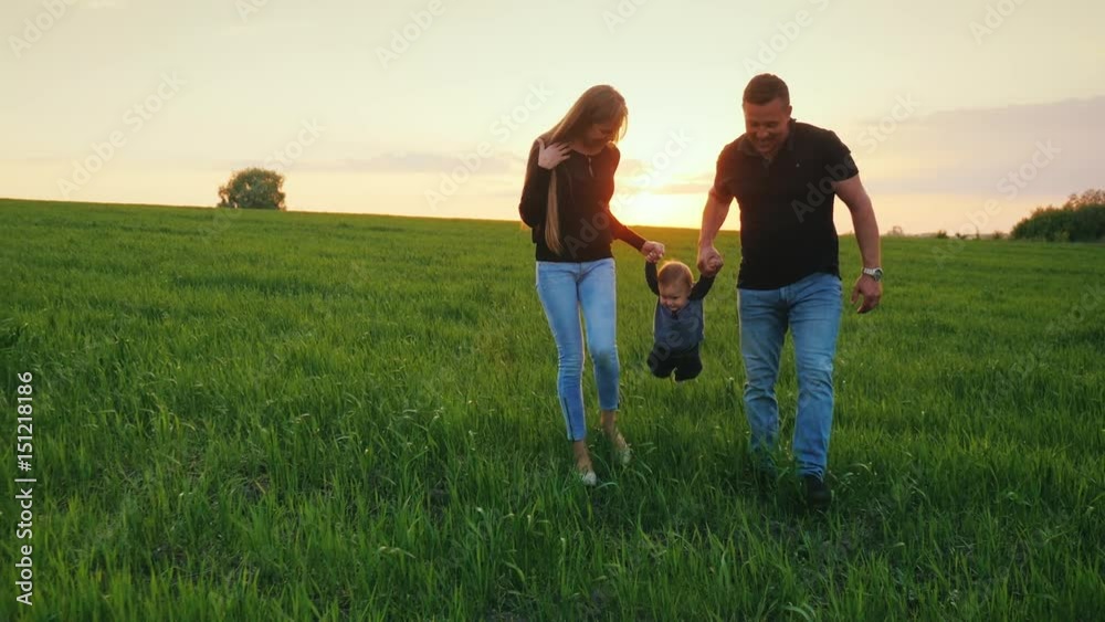 A happy couple of parents with a small son are walking across the field towards the sunset. Happy family with a child A happy couple of parents with a small son are walking across the field towards the sunset. Happy family with a child