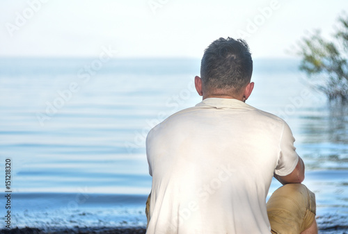 A young guy sits and stares into the distance on the seashore