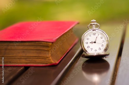 vintage gold pocket watch with red book on old wooden table