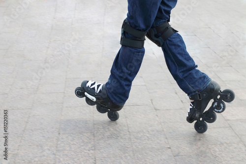 Young man wearing roller skates and protective knee pads riding on a city tile