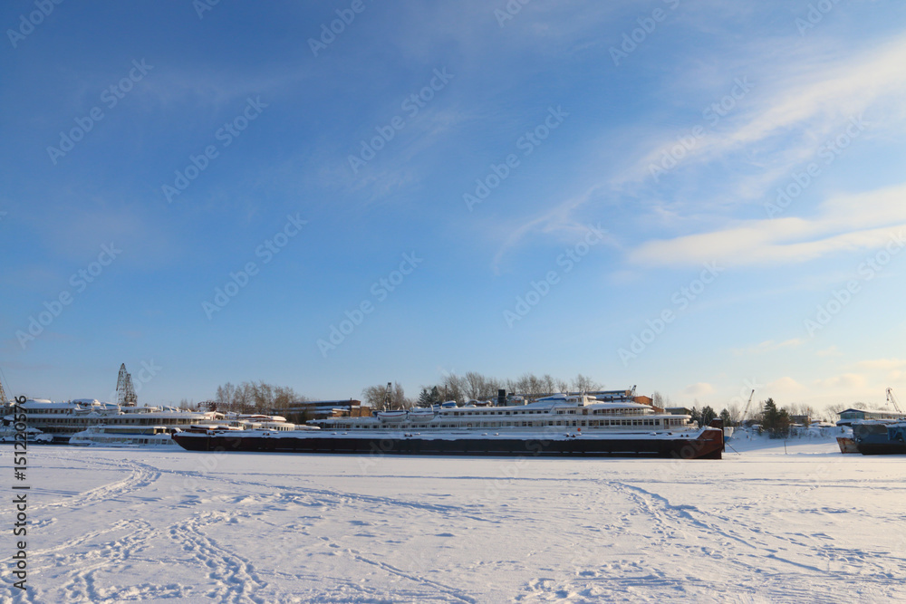 Passenger and cargo shipы in frozen river and cranes in winter sunny day