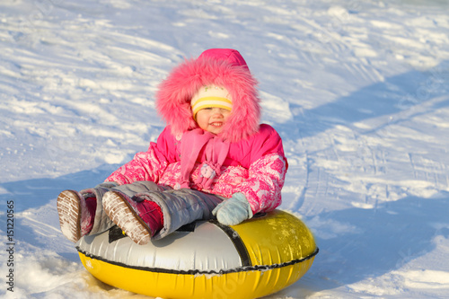 Little girl slides on snowtube down from hill at sunny winter day