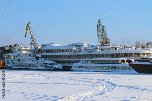 White beautiful passenger ship in frozen river and cranes in winter sunny day