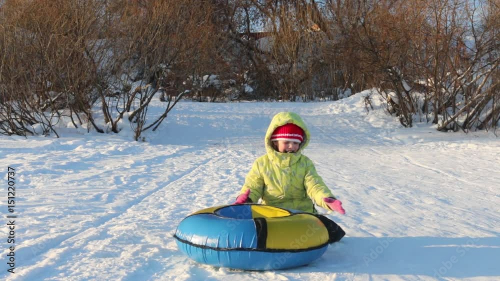 Girl plays with snowtube and hides behind it at hill at sunny winter day Girl plays with snowtube and hides behind it at hill at sunny winter day