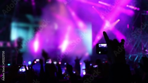 Hand with cell phone at concert with laser show and illumination, focus on hand