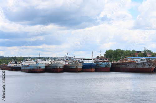 River with many rusty cargo ships and sky with clouds on summer day