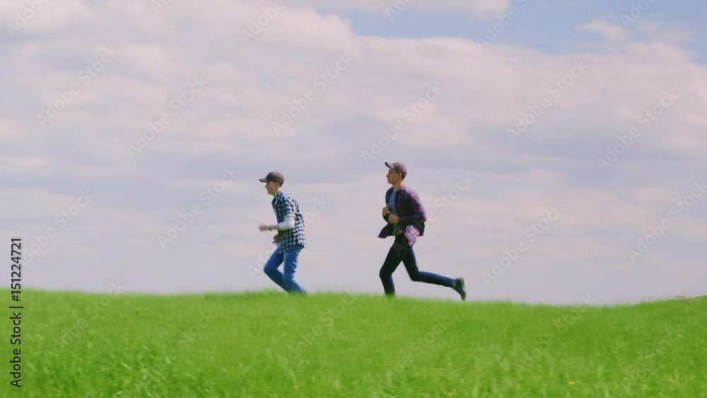 Two young teenage boys run along the green hill Two young teenage boys run along the green hill