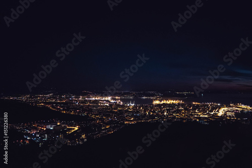 Blurred lights of night Trieste city landscape. Europe, Italy, Trieste city glowing night lights, Mediterranean port. Top view from hill viewpoint.