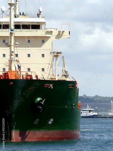 Closeup of vertical half part of a Tankership with details of wheelhouse, castle and main deck. Coastline and cloudy sky in background. Vertical front view. photo