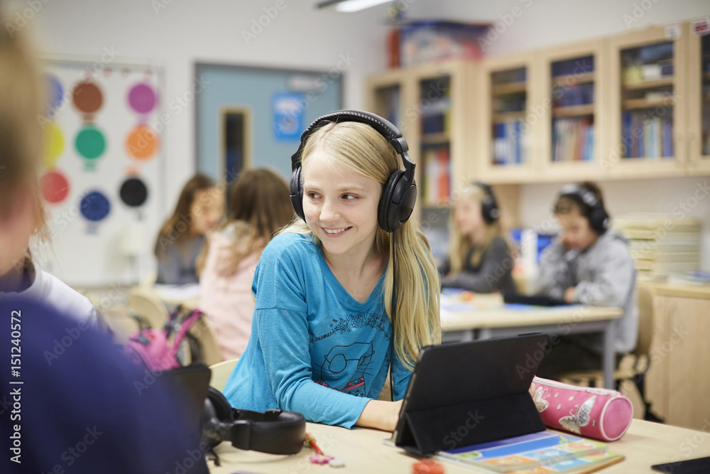 Smiling girl wearing headphones while using digital table in classroom Smiling girl wearing headphones while using digital table in classroom
