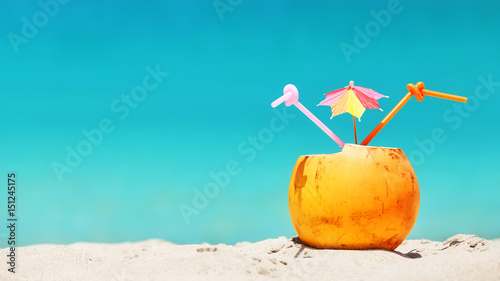 Coconut with straws and colorful cocktail umbrella on a tropical beach, summer holiday concept, selective focus, space for text.