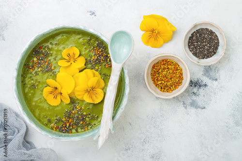 Breakfast detox green smoothie bowl topped with superfoods, chia seeds, bee pollen and edible flowers. Overhead, top view, flat lay, copy space