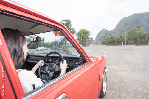Asian woman driving red car to tropical forest.