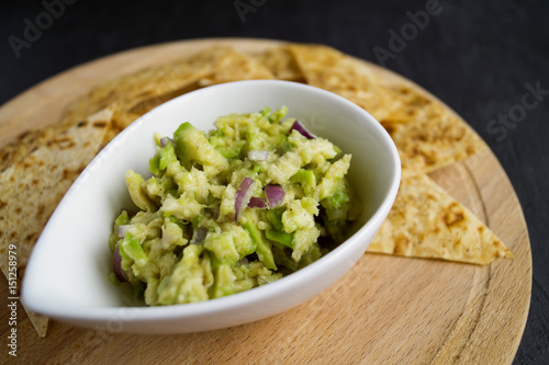 Green homemade Guacamole with chips. black background