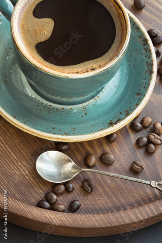 Cup of black coffee with coffee beans on wooden tray.
