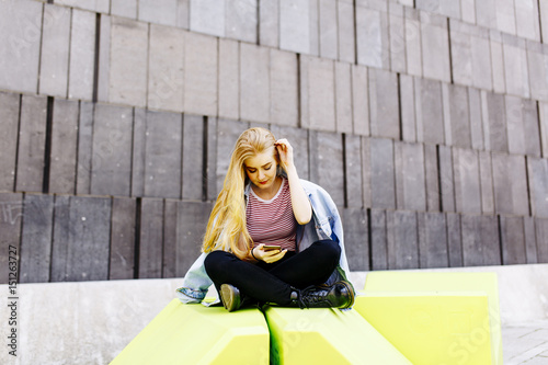 Urban young female student sitting outside and use the phone