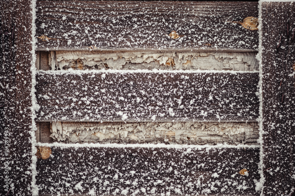 A wooden pallet covered with snow. Dry yellow autumn leaves.