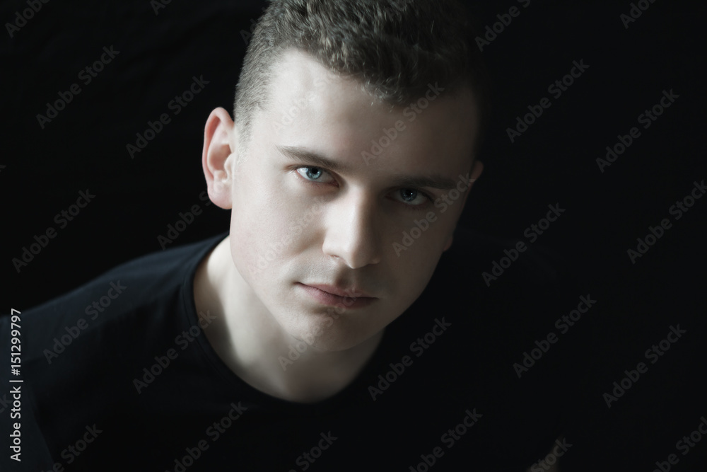 Headshot of confident young man is looking at camera in low-key lighting Headshot of confident young man is looking at camera in low-key lighting