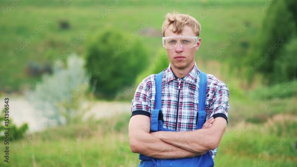 Portrait of a serious man in overalls in nature. Young attractive serious man looking at the camera in the meadow. Handheld shot. Portrait of a serious man in overalls in nature. Young attractive serious man looking at the camera in the meadow. Handheld shot.