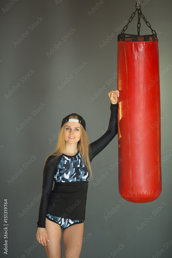 Shapely beautiful girl in sports clothes, standing leaning on a boxing pear
