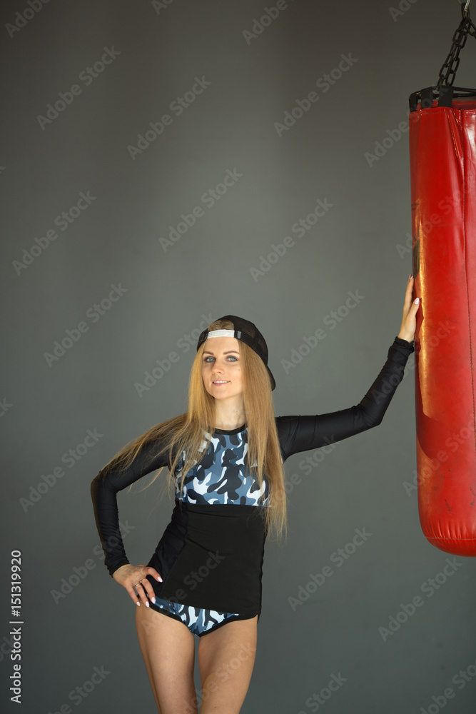 Shapely beautiful girl in sports clothes, standing leaning on a boxing pear