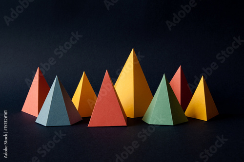 Multicolor geometric abstract background. Bright prism pyramid triangle shape figures on dark paper. Violet yellow blue pink green red color objects.