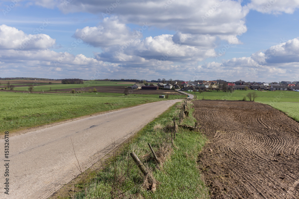 The road, the plowed field, the meadow and the village on the hill. Houses, dairy farms, barns. Early Spring on Podlasie, Eastern Poland.