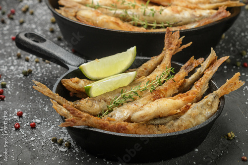 Fried smelt in a frying pan on the table with spices, lime and thyme. Small crispy fish. Selective focus