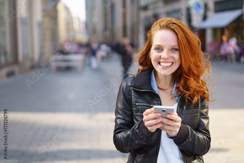 Fotografie lachende frau steht in der einkaufsstraße und hält ihr handy in der hand