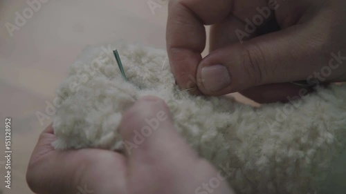 Wallpaper Mural Hands of the seamstress hold the needle and the part. The process of sewing together parts of a soft toy. Needles and safety pins are seamstress tools. The master makes a collectible toy teddy bear Torontodigital.ca