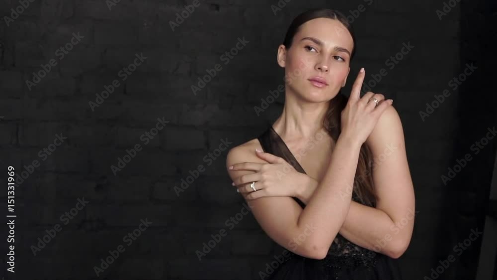 Beautiful brunette in a black dress posing and looking at the camera on a black wall background. Beautiful brunette in a black dress posing and looking at the camera on a black wall background.