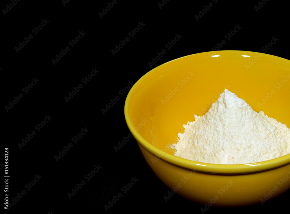 White dry flour in yellow ceramic bowl on black background with free space for text and design White dry flour in yellow ceramic bowl on black background with free space for text and design