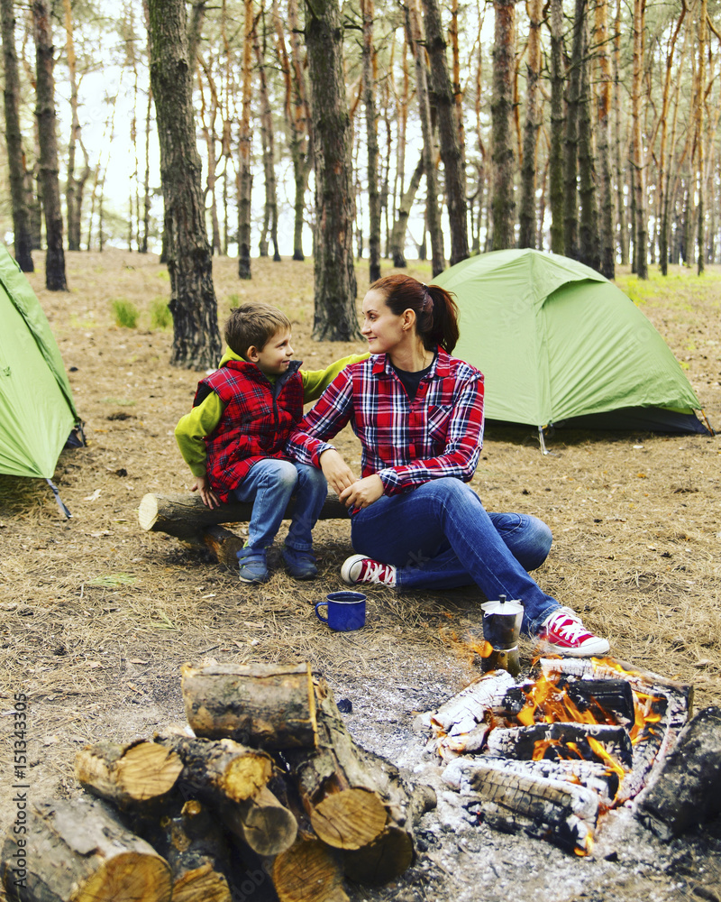 Camping in the forest. Mom and son are sitting near the fire preparing coffee and looking at the map. Camping in the forest. Mom and son are sitting near the fire preparing coffee and looking at the map.