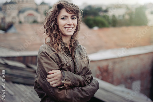 Young attractive woman with good mood enjoying beautiful city landscape while standing on a roof of building, charming smiling hipster girl relaxing after excursion during her amazing spring weekend © Andrii