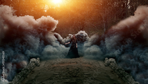Young attractive Witch walking on the bridge in heavy black smoke. photo
