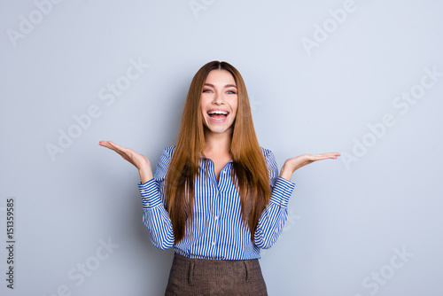 Cheerful charming girl in formal wear on pure background is gesturing with hands like she is holding something and need to choose between two options