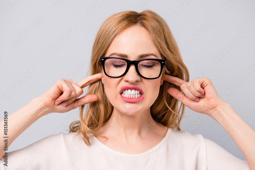 Angry pretty young woman in spectacles covering her ears with fingers and showing teeth Angry pretty young woman in spectacles covering her ears with fingers and showing teeth
