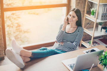 Young pretty smiling woman at workplace  talking on phone while having a rest at work. Intentional sun glare, lens flares effect
