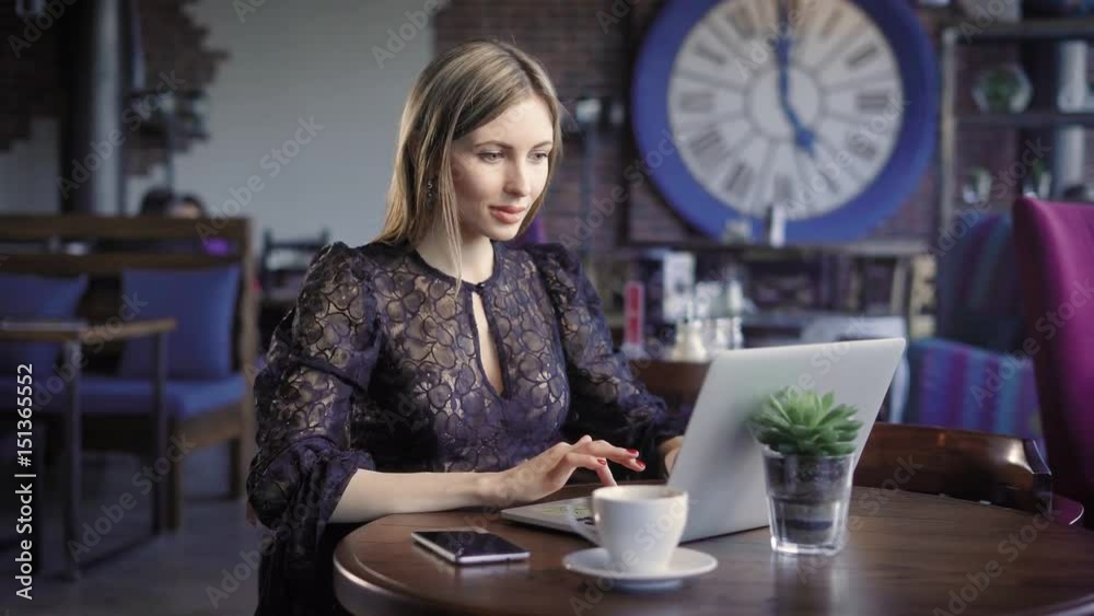 A woman who sits in a lonely restaurant during the day looks at a dating site on a laptop, responding to fan messages, next to her is a cup of coffee