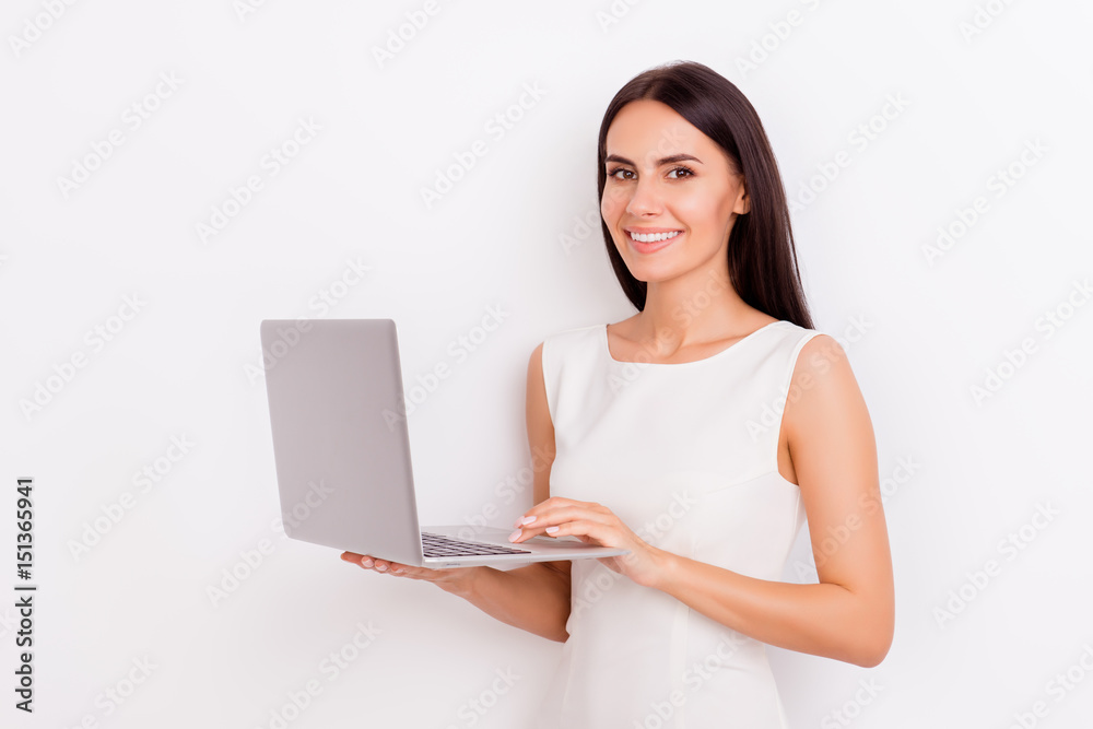 Young smiling attractive brunette girl is holding laptop and typing on it. She is smiling, wearing white clothes and behind her is a pure background Young smiling attractive brunette girl is holding laptop and typing on it. She is smiling, wearing white clothes and behind her is a pure background