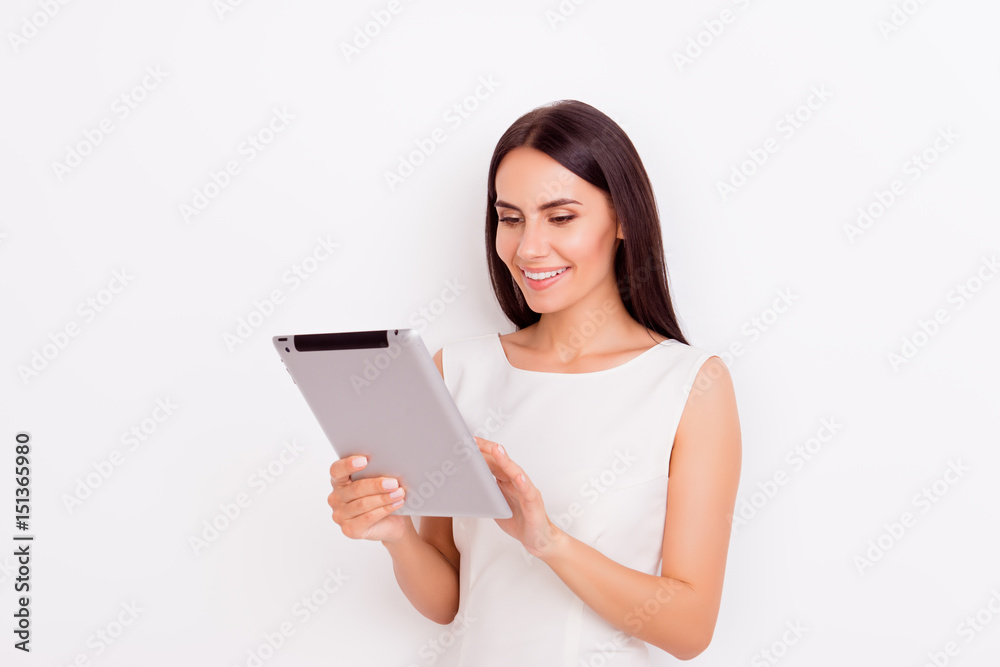 Gorgeous young brunette is holding laptop and browsing info on it. She is smiling, wearing white outfit and behind her is a pure background Gorgeous young brunette is holding laptop and browsing info on it. She is smiling, wearing white outfit and behind her is a pure background