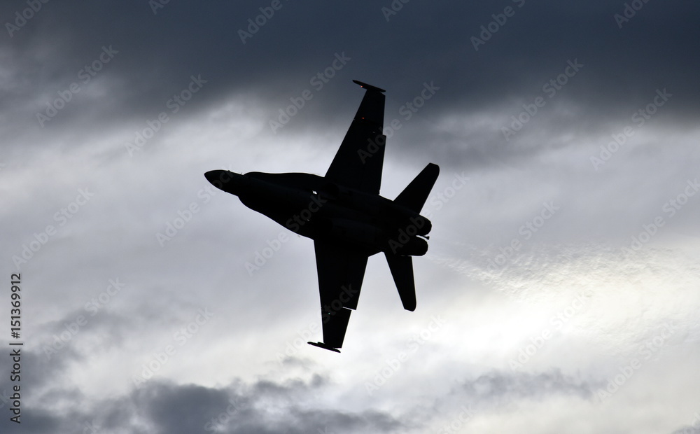 Silhouette of F18 Hornet fighter aircraft in flight. Clouds in the background.