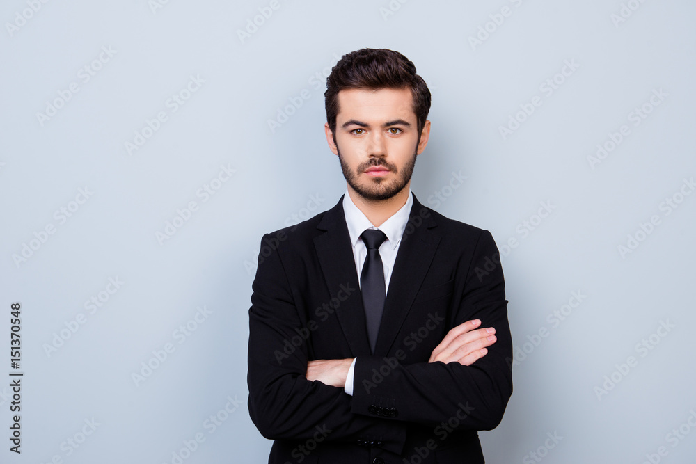 Portrait of handsome strict employer in formal clothes standing with crossed hands against gray background Portrait of handsome strict employer in formal clothes standing with crossed hands against gray background