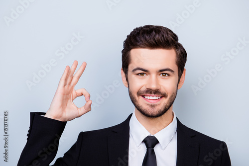 Confident young smiling smart-clothed freelancer showing ok-sign on gray background